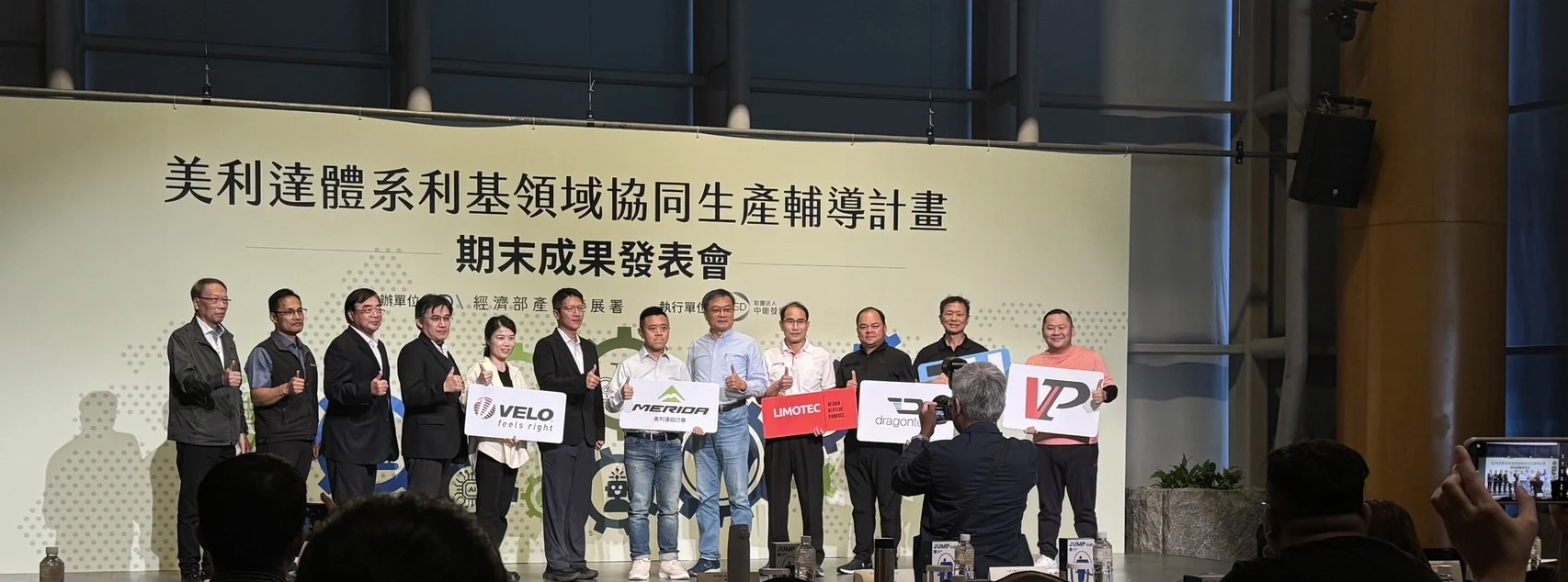 美利達體系利基領域協同生產輔導計畫期末成果發表會，協力廠代表於台上合影，背板為經濟部產業發展署主辦、中衛發展中心執行