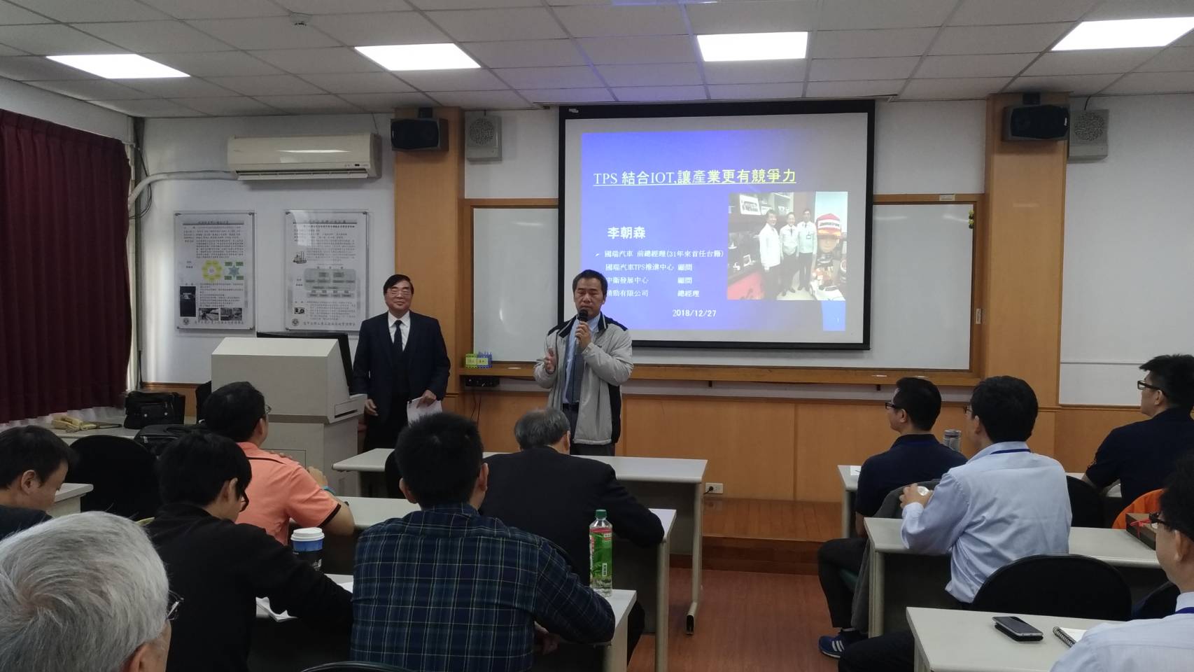 2018 年 12 月 27 日演講現場，螢幕投影片標題為「TPS 結合 IOT,讓產業更有競爭力」，講者李朝森，投影片並列其國瑞汽車前總經理、國瑞汽車 TPS 推進中心顧問、中衛發展中心顧問、精勁有限公司總經理四個身分